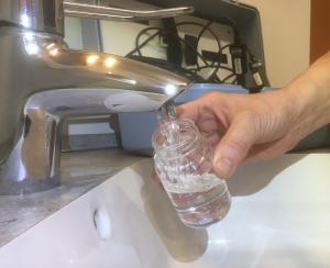 Wasser läuft aus dem Wasserhahn in ein steriles Probennahmeglas zur Überprüfung der mikrobiologischen Trinkwasserqualität.