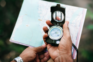 Ein Mann hält einen Kompass in der Hand, im Hintergrund eine Landkarte
