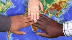 Auf einer Weltkarte sieht man drei Händeübereiander mit unterschiedlicher Hautfarbe.