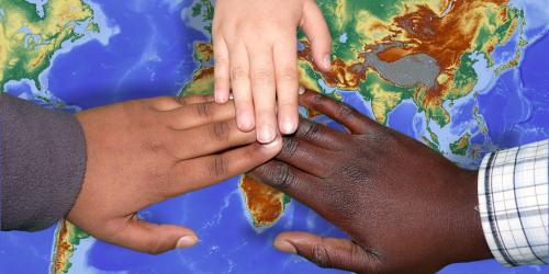 Auf einer Weltkarte sieht man drei Händeübereiander mit unterschiedlicher Hautfarbe.