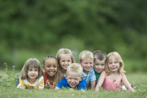 7 Kinder liegen auf einer Wiese und schauen in die Kamera
