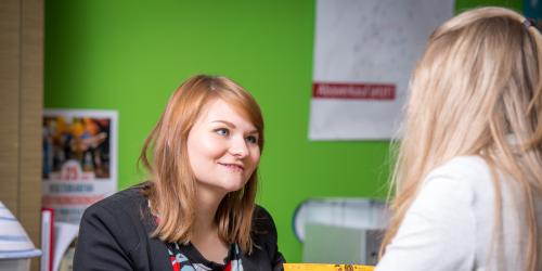Eine Mitarbeiterin der Jena Tourist-Information verkauft einer jungen Frau ein Ticket.