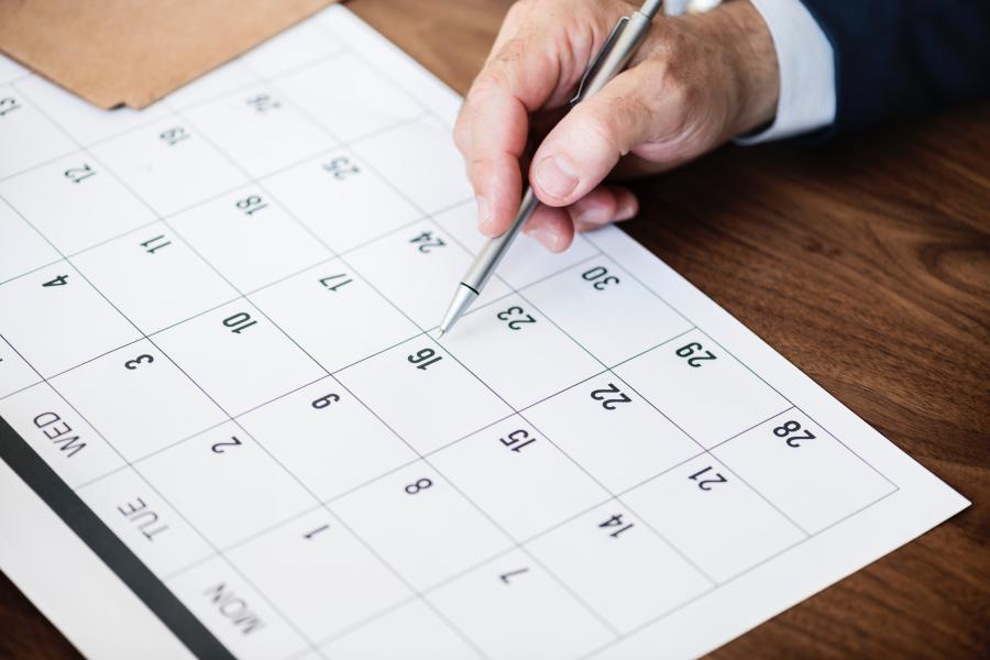 Hand mit Stift die auf einen Papierkalender zeigt.